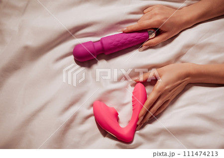 sex vibrator and vacuum stimulator in a woman girl hand on a white sheet on bed in bedroom. Sex toys for female satisfaction and orgasm sex vibrator and vacuum stimulator in a woman girl hand on a white sheet on bed in bedroom. Sex toys for female satisfaction and orgasm 111474213