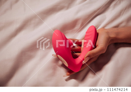 pink vibrator vacuum stimulator in a woman hand on a white sheet on the bed in bedroom. Sex toys for female satisfaction and orgasm pink vibrator vacuum stimulator in a woman hand on a white sheet on the bed in bedroom. Sex toys for female satisfaction and orgasm 111474214