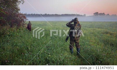 Huntsman and hunter look through binoculars through the fog at wild ungulates. Huntsman and hunter look through binoculars through the fog at wild ungulates. 111474951