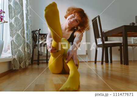 Young woman in bright yellow tights sits on parquet floor at home 111477671