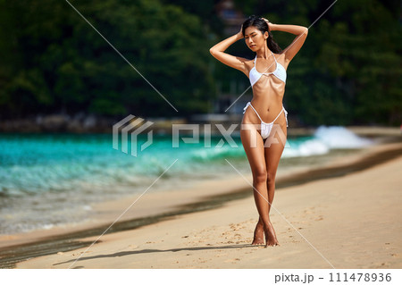Beautiful asian girl in white bikini posing at the tropical beach Beautiful asian girl in white bikini posing at the tropical beach 111478936