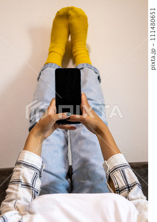 Woman with feet up using phone at home in a relaxing moment 111480651