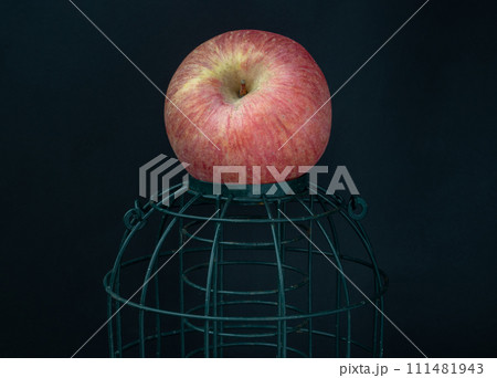 A lonely apple put on a green cage on Dark background. A lonely apple put on a green cage on Dark background. 111481943