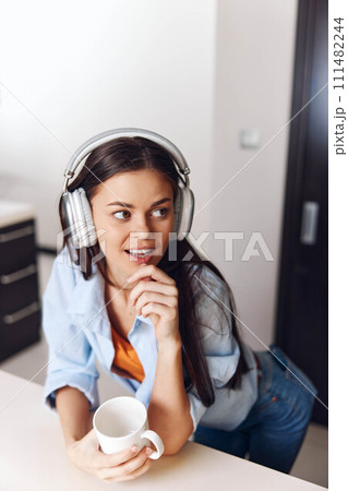 Young woman enjoying music and coffee at home, wearing headphones and looking relaxed and beautiful in cozy setting 111482244