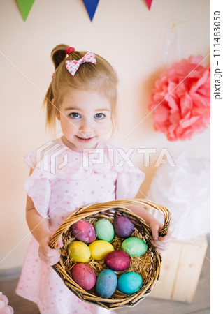 Cute little girl wearing pink dress holding basket with painted Easter eggs 111483050