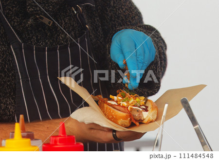 Chef making hot dog for a customer at farmers market. Chef making hot dog for a customer at farmers market. 111484548