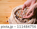 Hands scooping diverse colorful heirloom beans from a rustic eco bag. Whole foods and healthy eating in sustainable packaging 111484756