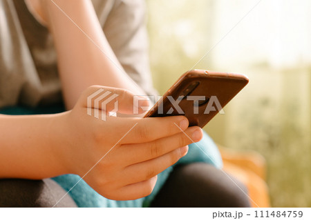 Close-up of hands holding a smartphone, Person texting message on Smartphone, with blurred background in warm natural light. Mobile technology in everyday life. Social media interaction 111484759