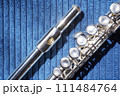 Close-up of silver flute with detailed view of mouthpiece, shiny surface and keys of instrument on blue fabric background, emphasizes the flute's elegance. Instrument maintenance and care 111484764