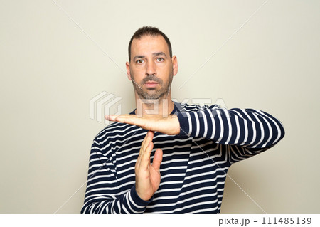 Bearded Hispanic man in his 40s wearing a striped sweater calling for a time out with his hands isolated on a beige background, he needs a break from the fast pace of his life. Bearded Hispanic man in his 40s wearing a striped sweater calling for a time out with his hands isolated on a beige background, he needs a break from the fast pace of his life. 111485139