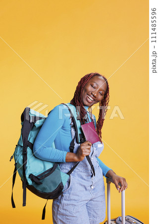 Smiling adult with passport on camera, feeling excited about international vacation destination. Cheerful woman preparing to board airplane, carrying luggage and identification pass. 111485596