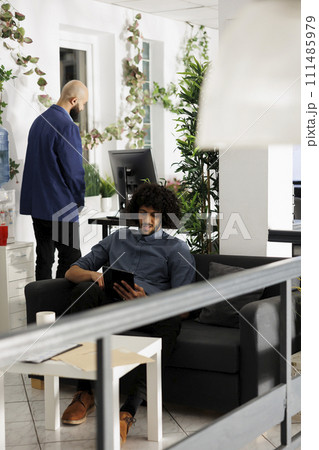 Arab start up company worker using digital tablet during work break while sitting on couch. Young entrepreneur chatting in social media network in business open space office 111485979