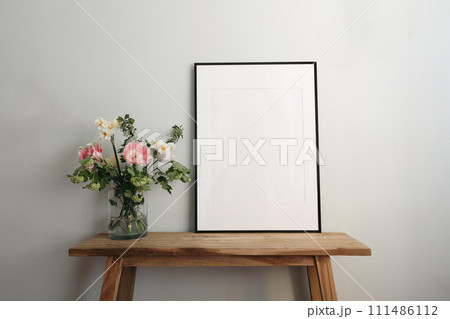 Easter springtime still life. Blank black picture frame mockup on wooden bench, table. Spring bouquet of pink tulips, white daffodils, hawthorn flowers. Pastel green, mint wall background. Easter springtime still life. Blank black picture frame mockup on wooden bench, table. Spring bouquet of pink tulips, white daffodils, hawthorn flowers. Pastel green, mint wall background. 111486112
