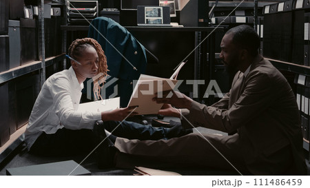 Law inspectors doing background checks with records, analyzing evidence in case files to find suspect and solve felony. Team of private investigators examining surveillance photos in incident room. Law inspectors doing background checks with records, analyzing evidence in case files to find suspect and solve felony. Team of private investigators examining surveillance photos in incident room. 111486459