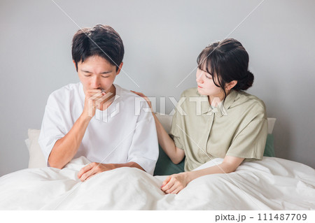 朝寝室で咳・風邪に悩む男性と心配する女性・夫婦・カップル 111487709