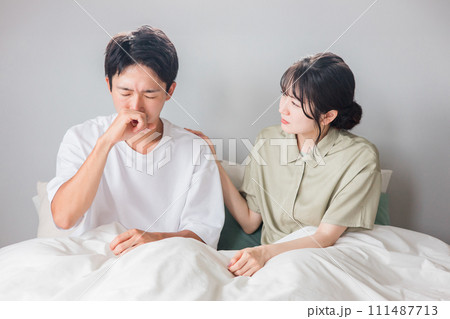 朝寝室で花粉症・鼻炎・鼻水に悩む男性と心配する女性・夫婦・カップル 111487713
