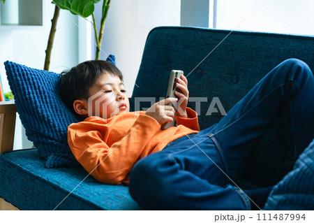 ソファーに寝転んでスマホを使う男子小学生 111487994