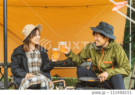 秋冬のキャンプ場でキャンプ飯を作って乾杯する男女のキャンパー 秋冬のキャンプ場でキャンプ飯を作って乾杯する男女のキャンパー 111488215