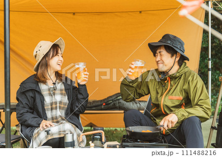 秋冬のキャンプ場でキャンプ飯を作って乾杯する男女のキャンパー 秋冬のキャンプ場でキャンプ飯を作って乾杯する男女のキャンパー 111488216