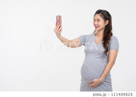 Happy Asian Pregnant Woman standing video call conference on mobile phone with family or selfie isolated on white background. Pregnancy of young woman enjoying with future life Happy Asian Pregnant Woman standing video call conference on mobile phone with family or selfie isolated on white background. Pregnancy of young woman enjoying with future life 111489828