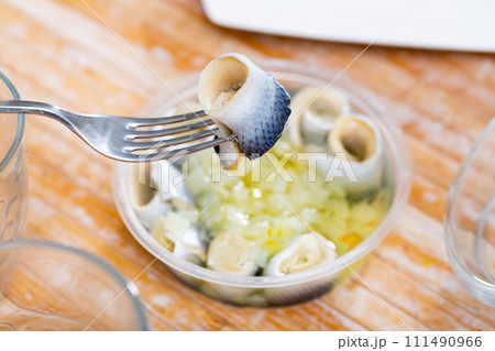 Invisible hand holds fork with pierced piece of salted herring fillet Invisible hand holds fork with pierced piece of salted herring fillet 111490966