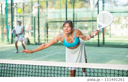 Young woman hitting ball with left-handed forehand while playing padel 111491261