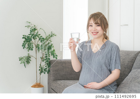 家のソファで水・ぬるま湯・白湯を飲む妊婦の女性・マタニティ・プレママ 家のソファで水・ぬるま湯・白湯を飲む妊婦の女性・マタニティ・プレママ 111492695