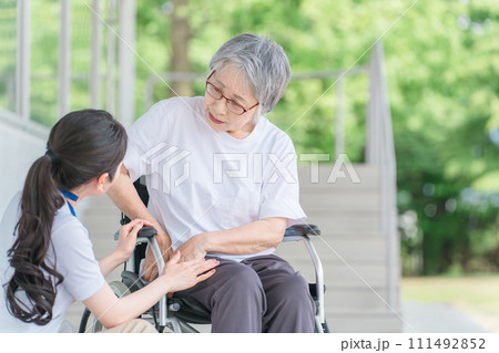 車椅子に乗る股関節が痛い高齢者と介護士の女性（リウマチ・人工関節） 111492852