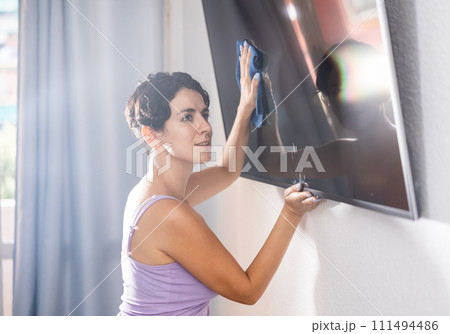Positive brunette woman cleaning dust from TV screen Positive brunette woman cleaning dust from TV screen 111494486