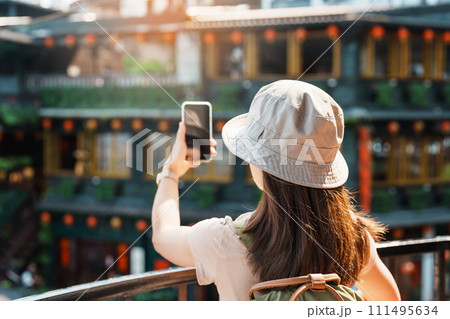 woman traveler visiting in Taiwan, Tourist taking photo and sightseeing in Jiufen Old Street village with Tea House background. landmark and popular attractions near Taipei city. Travel concept 111495634