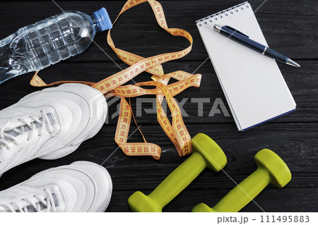 Athlete's set with female clothing, equipment, bottle of water and notebook on wooden background. Athlete's set with female clothing, equipment, bottle of water and notebook on wooden background. 111495883
