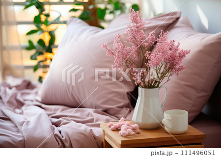 Pink flowers in a white ceramic vase on the bedside table against the background of a bed with pink bed linen Pink flowers in a white ceramic vase on the bedside table against the background of a bed with pink bed linen 111496051