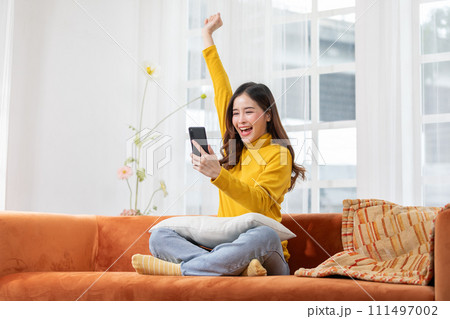 Millennial asian young woman looking mobile phone laughing with good news or discount voucher for shopping online at home.Happy and cheerful woman looking on cellphone app read message feel excited Millennial asian young woman looking mobile phone laughing with good news or discount voucher for shopping online at home.Happy and cheerful woman looking on cellphone app read message feel excited 111497002