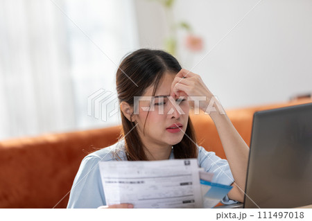 Young Asian woman looks stressed while examining a bill, impactful financial pressure, anxiety, and the challenges of managing expenses. Financial problem. Young Asian woman looks stressed while examining a bill, impactful financial pressure, anxiety, and the challenges of managing expenses. Financial problem. 111497018