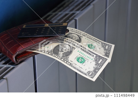 Calculator, wallet and banknotes lie on the radiator of the heating system, the cost of heat Calculator, wallet and banknotes lie on the radiator of the heating system, the cost of heat 111498449