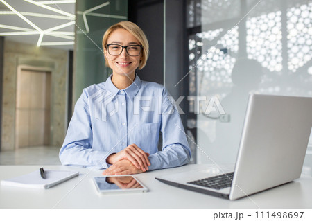 Satisfied woman with short haircut folding hands on desk with computer and notebook with pen. Smiling hr manager getting ready for interview and welcoming new candidate for position in company 111498697