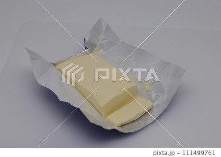 Cut block of fresh butter with wrapper on white background. 111499761