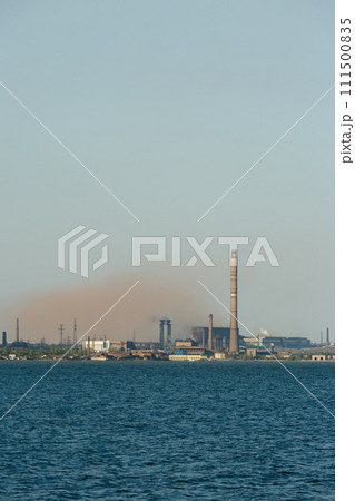 Industrial skyline dominated by a metallurgical plants tall chimneys emitting smoke over a body of water, symbolizing industrial pollution and eco awareness issues. 111500835