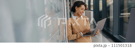 Stylish business woman using laptop while standing on modern office background Stylish business woman using laptop while standing on modern office background 111501318