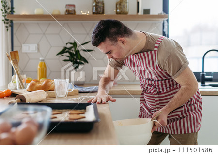 Young man with Down syndrome baking cookies at home. Everyday routine for man with Down syndrome. Young man with Down syndrome baking cookies at home. Everyday routine for man with Down syndrome. 111501686