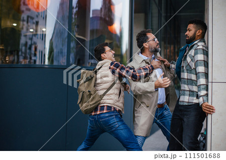 Angry man is aggressive, have conflict with young man, holding him by shirt, screaming, threatening him. Friend helping to end fight. Angry man is aggressive, have conflict with young man, holding him by shirt, screaming, threatening him. Friend helping to end fight. 111501688