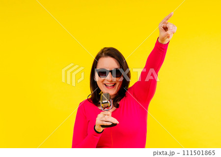 Woman in sport clothes sings into a wired microphone and claps her hands on a yellow background Woman in sport clothes sings into a wired microphone and claps her hands on a yellow background 111501865