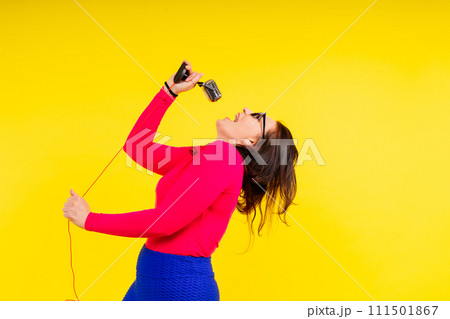 Woman in sport clothes sings into a wired microphone and claps her hands on a yellow background Woman in sport clothes sings into a wired microphone and claps her hands on a yellow background 111501867