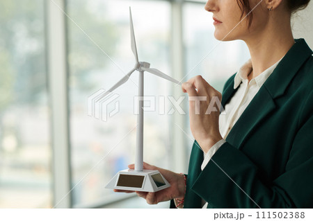 Cropped shot of young modern businesswoman in formalwear holding model of wind turbine representing usage of clean energy Cropped shot of young modern businesswoman in formalwear holding model of wind turbine representing usage of clean energy 111502388