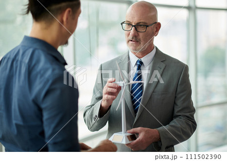 Mature entrepreneur with mockup of windmill making presentation to young subordinate, colleague or business partner at meeting Mature entrepreneur with mockup of windmill making presentation to young subordinate, colleague or business partner at meeting 111502390
