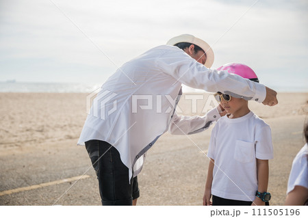 A family on vacation at the beach where the father sporting a safety helmet teaches his cheerful son the balance and joy of bicycle riding a memorable tourism day filled with family happiness. A family on vacation at the beach where the father sporting a safety helmet teaches his cheerful son the balance and joy of bicycle riding a memorable tourism day filled with family happiness. 111505196
