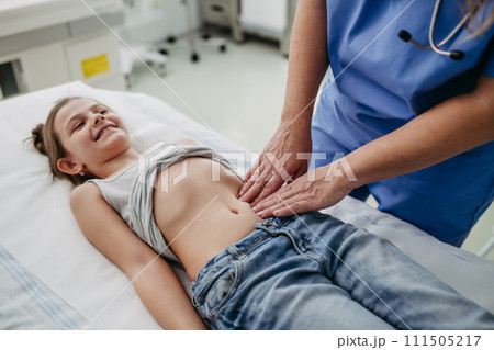 Close up of doctor palpating girl's abdomen, touching with hands and steady pressure on belly. Concept of preventive health care for children. 111505217