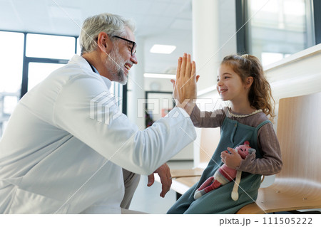 Friendly pediatrician giving high five to little patient. Cute preschool girl in greeting doctor in hospital corridor. 111505222
