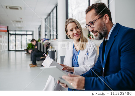 Pharmaceutical sales representative talking with doctor in medical building. Ambitious male sales representative presenting new medication on tablet. 111505486