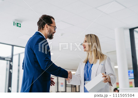 Pharmaceutical sales representative talking with doctor in medical building. Ambitious male sales representative presenting new medication on tablet. 111505504